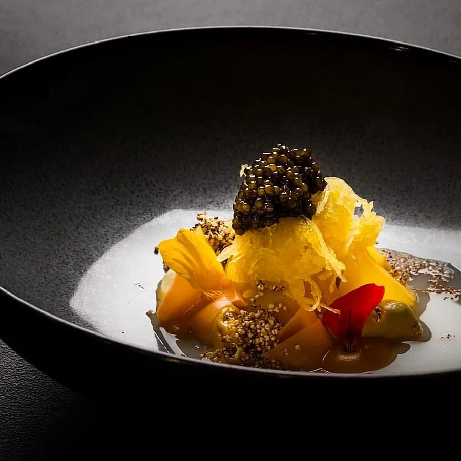 Caviar and yellow edible flowers on a dark ceramic plate